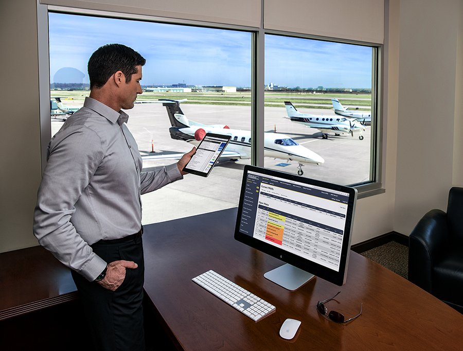 Man reviews iPad and computer in office with business jets outside