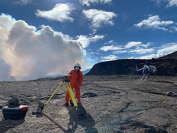 An HVO geophysicist deploys a GPS receiver on the Kilauea caldera floor to measure changes in ground motion. A volcanic gas plume rises in the background. (Photo: USGS)