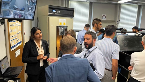 4.The top screen showing the hydrogen maser and cesium clocks in an adjacent isolated room used for realization of the timescale for research purposes. Students presenting their work to the USNO and Microchip Inc., visitors. (Photo: University of Alabama, Tuscaloosa)