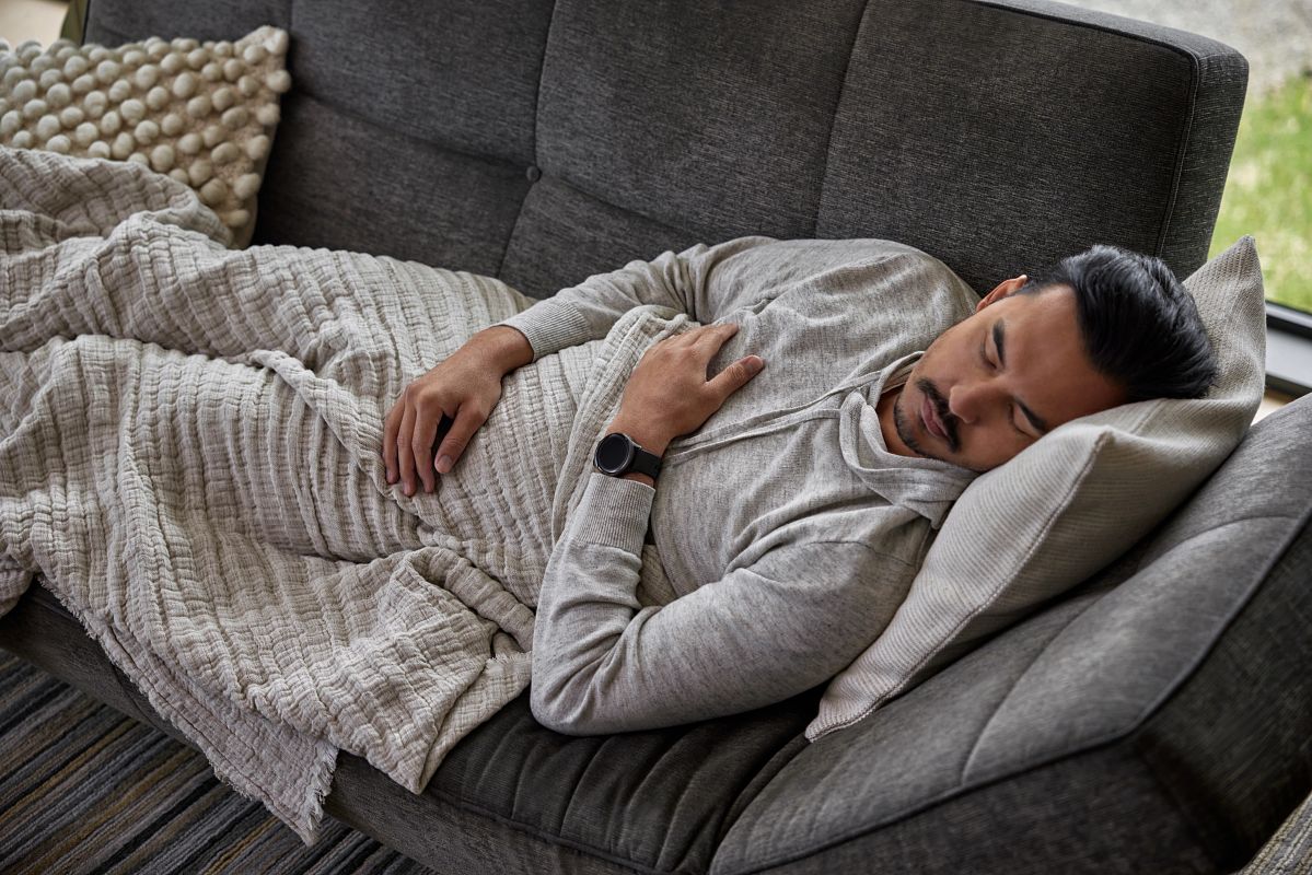 A man in a gray shirt naps on a dark gray couch.