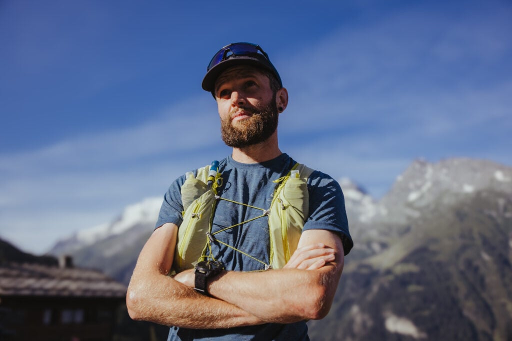 Jake Catterall, wearing a Garmin Enduro 2, stands with his arms crossed with mountains in the background.