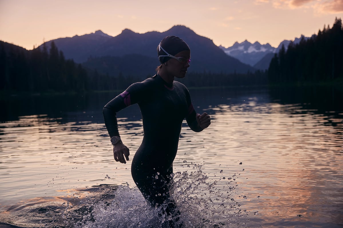 A triathlete runs during an open water transition with mountains in the background.