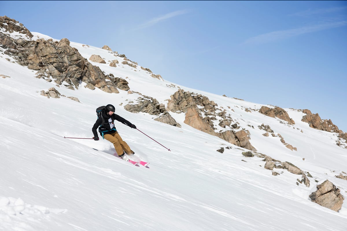 A person on pink skis and wearing a black helmet skis down a mountain covered in snow.