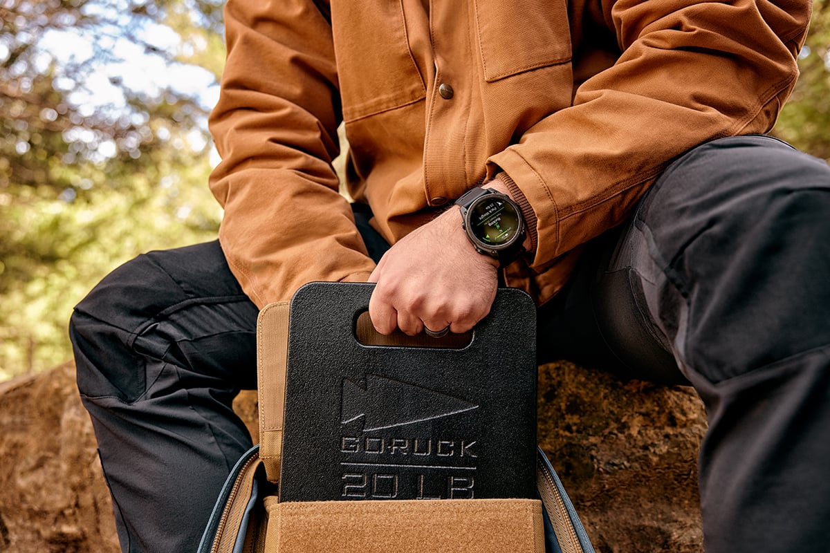 A man in a copper-colored jacket pulls a GORUCK weight out of his pack during a rucking activity.