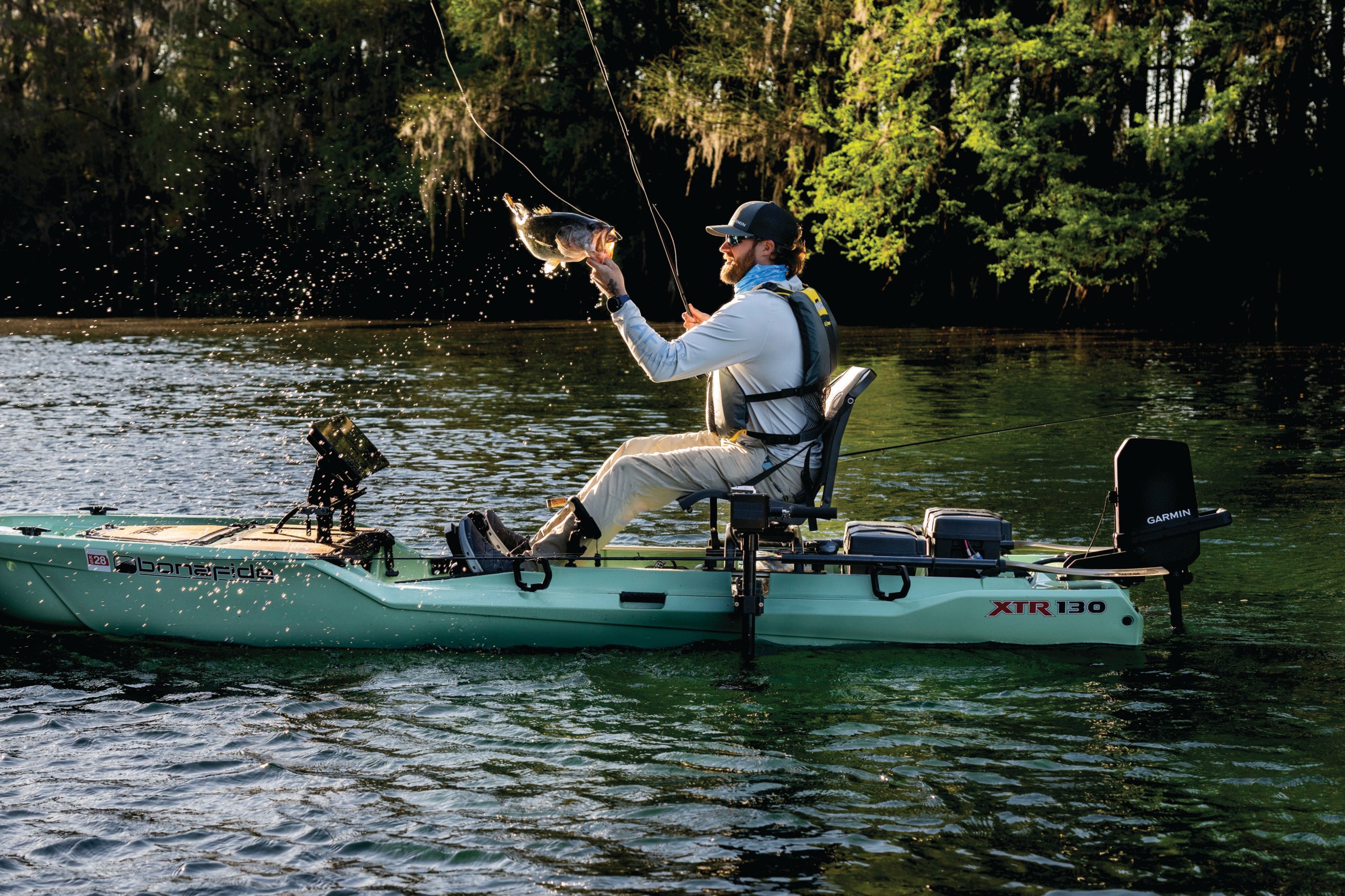 Person sitting on their kayak with a fish in hand and Force Current trolling motor on the back of the kayak.