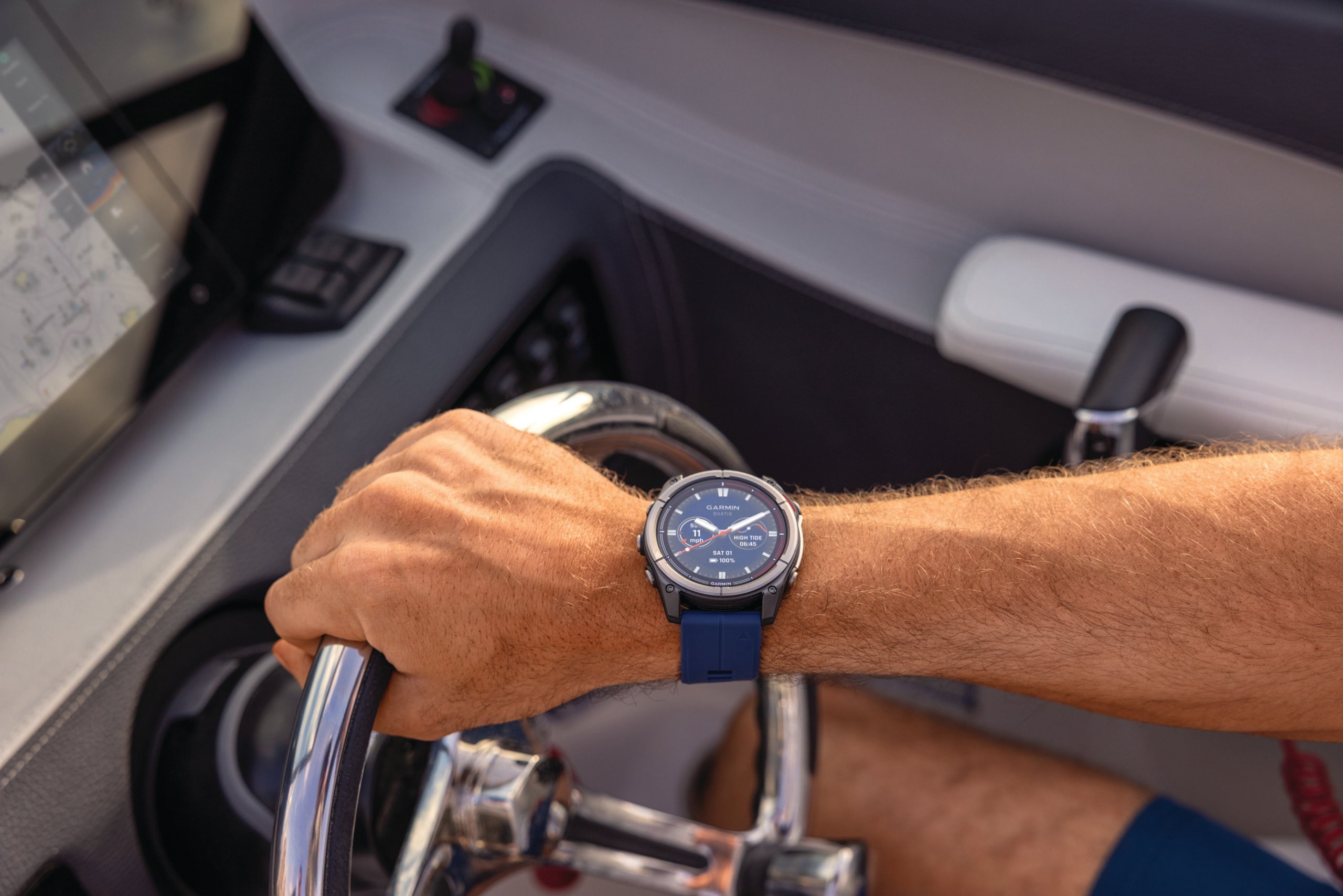 A persons hand on the steering wheel with a quatix 8 on their wrist.