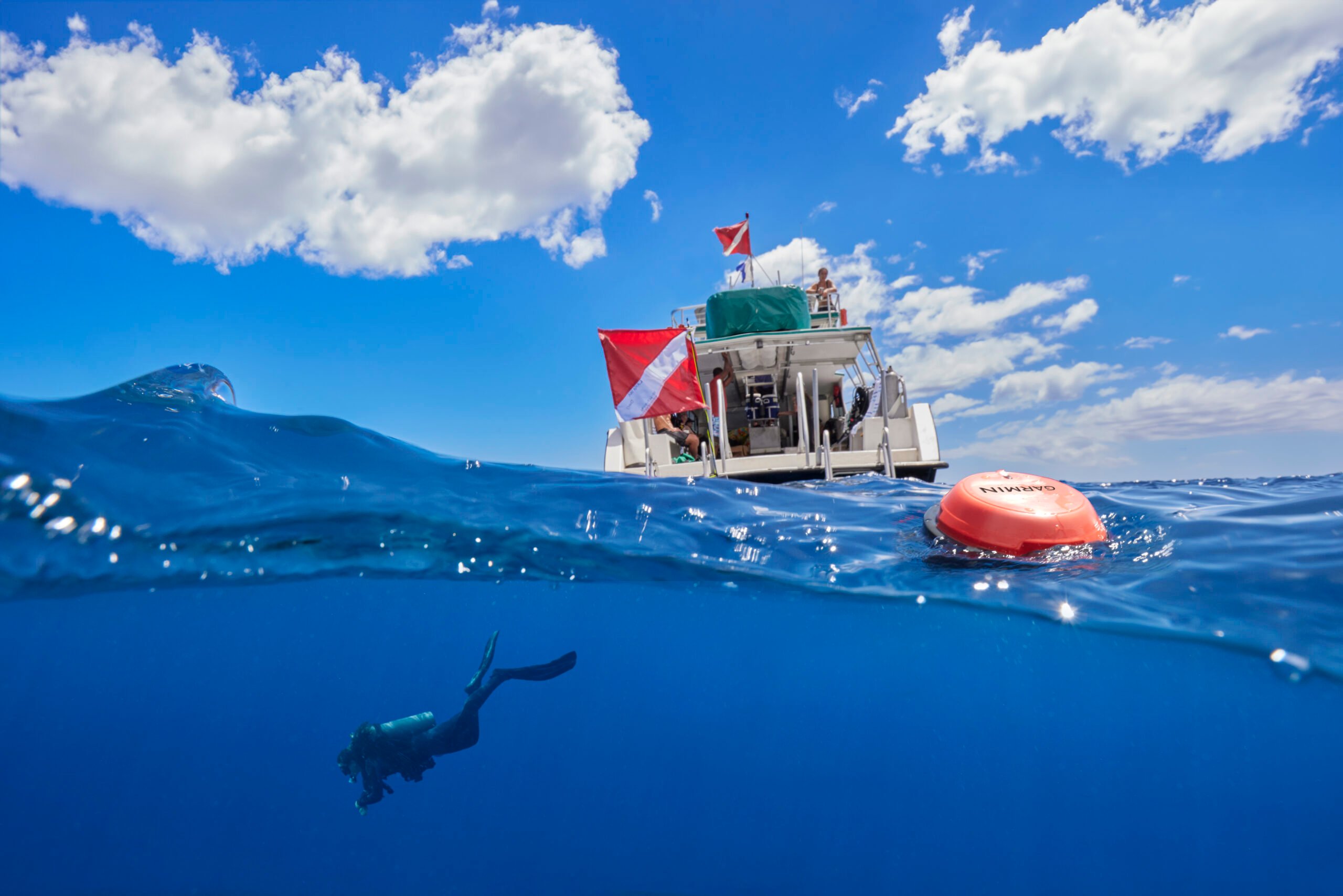 The crew sits atop a boat while a diver is in the water below them. The Descent S1 Buoy floats in between the two.