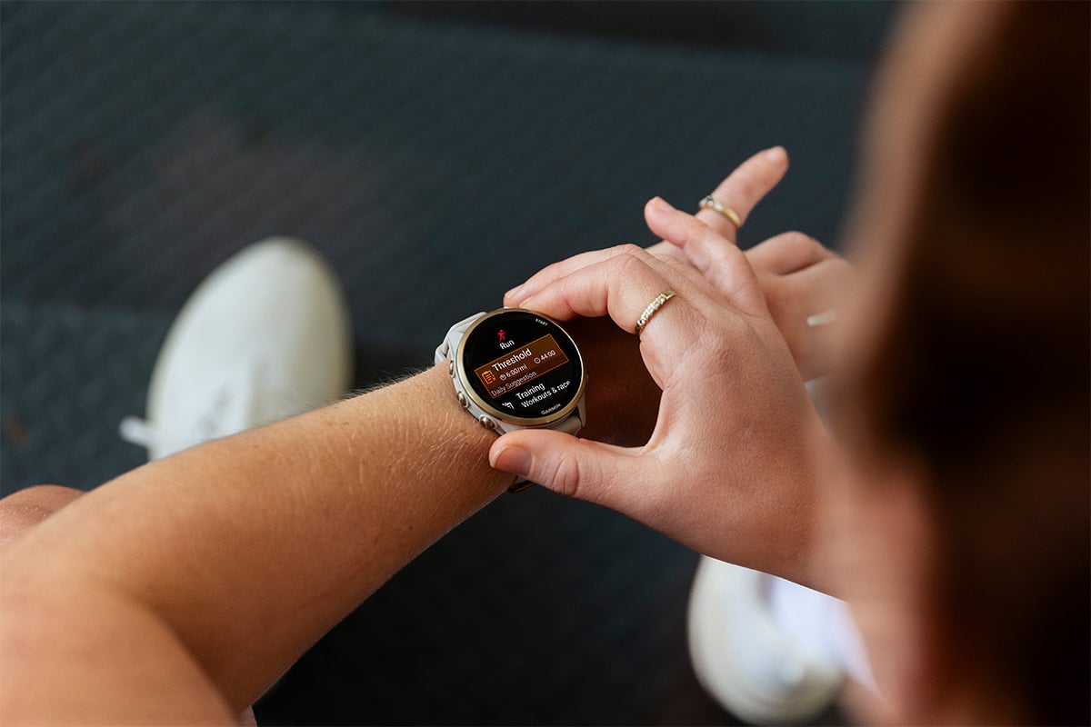 A woman wearing a Garmin Forerunner 970 GPS smartwatch looks at a threshold running activity for her daily suggested workout.