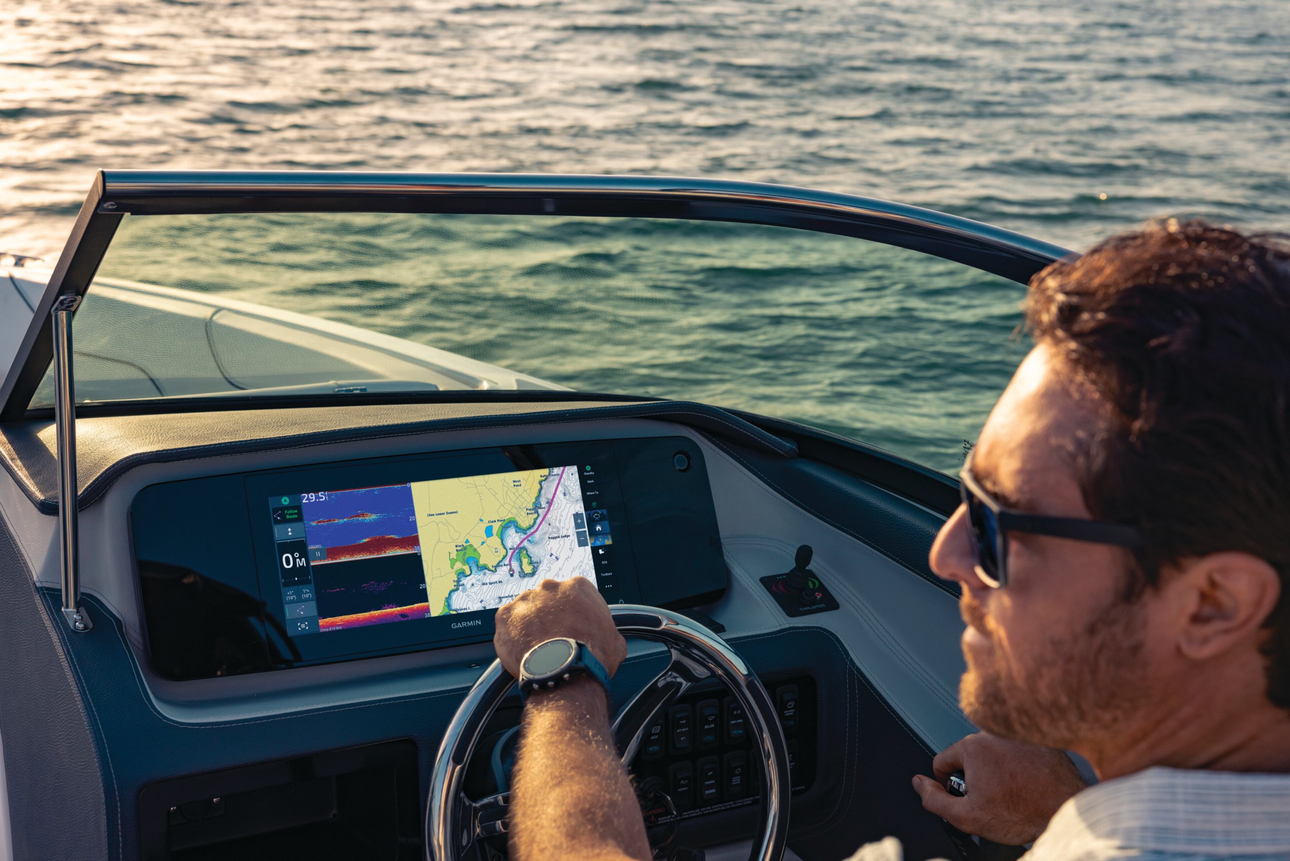 A man at the wheel of a boat with marine charts pulled up on the dashboard.