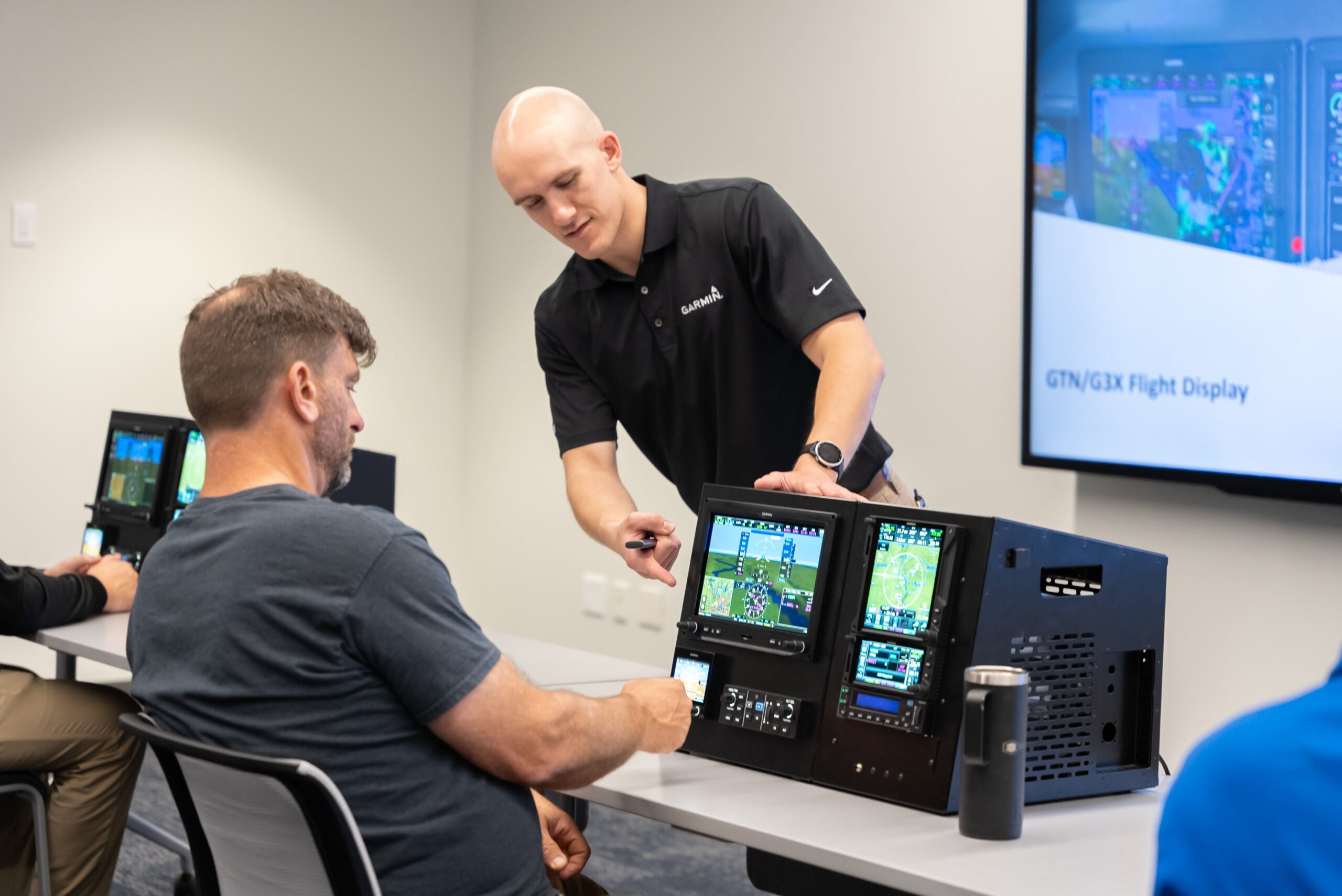 A Garmin aviation product support associate assists a person with training of a Garmin Integrated Flight Deck in a classroom setting.