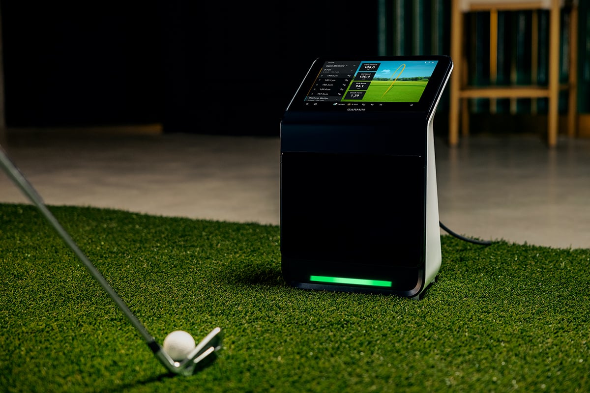 The Garmin Approach R50 launch monitor and simulator rests on top of turf in an indoor golf set up.