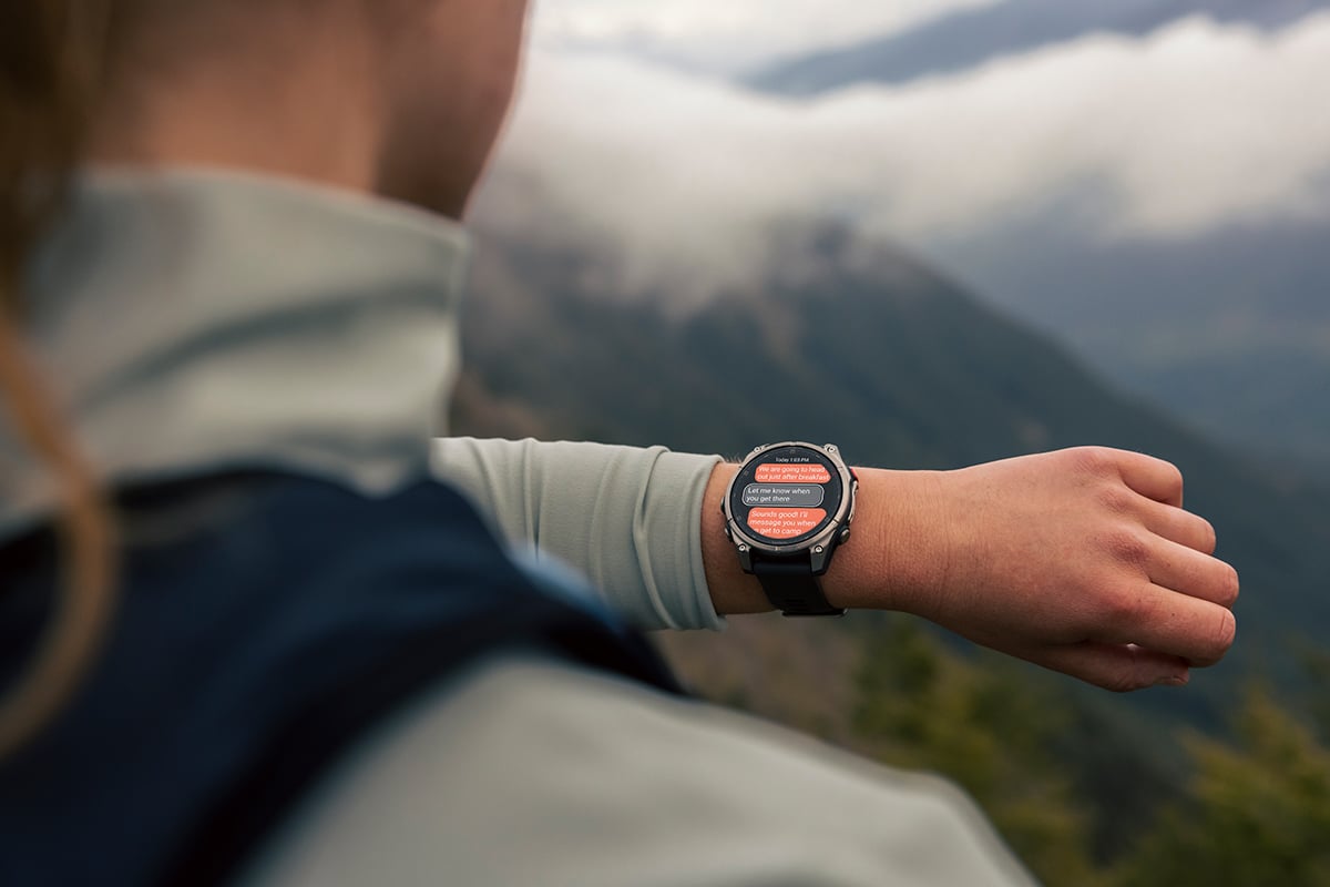 A woman wearing the Garmin fēnix 8 Pro smartwatch looks at the screen displaying messages about her trip.