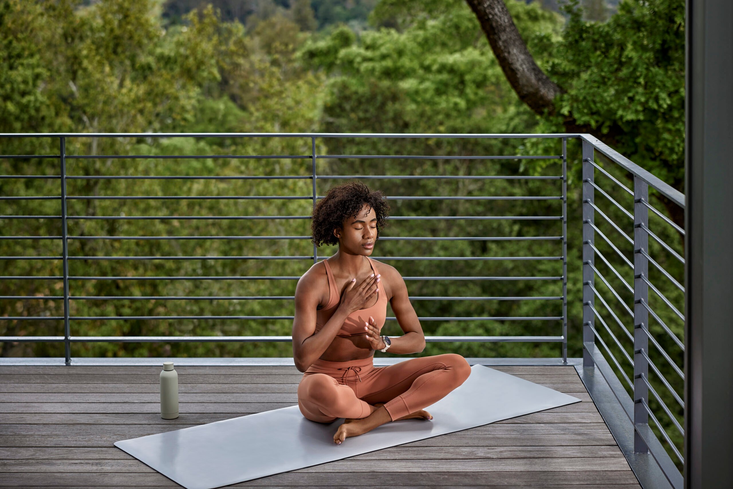 A woman sitting criss-cross on yoga mat. She has one hand on her heart and the other on her stomach taking a deep breath.