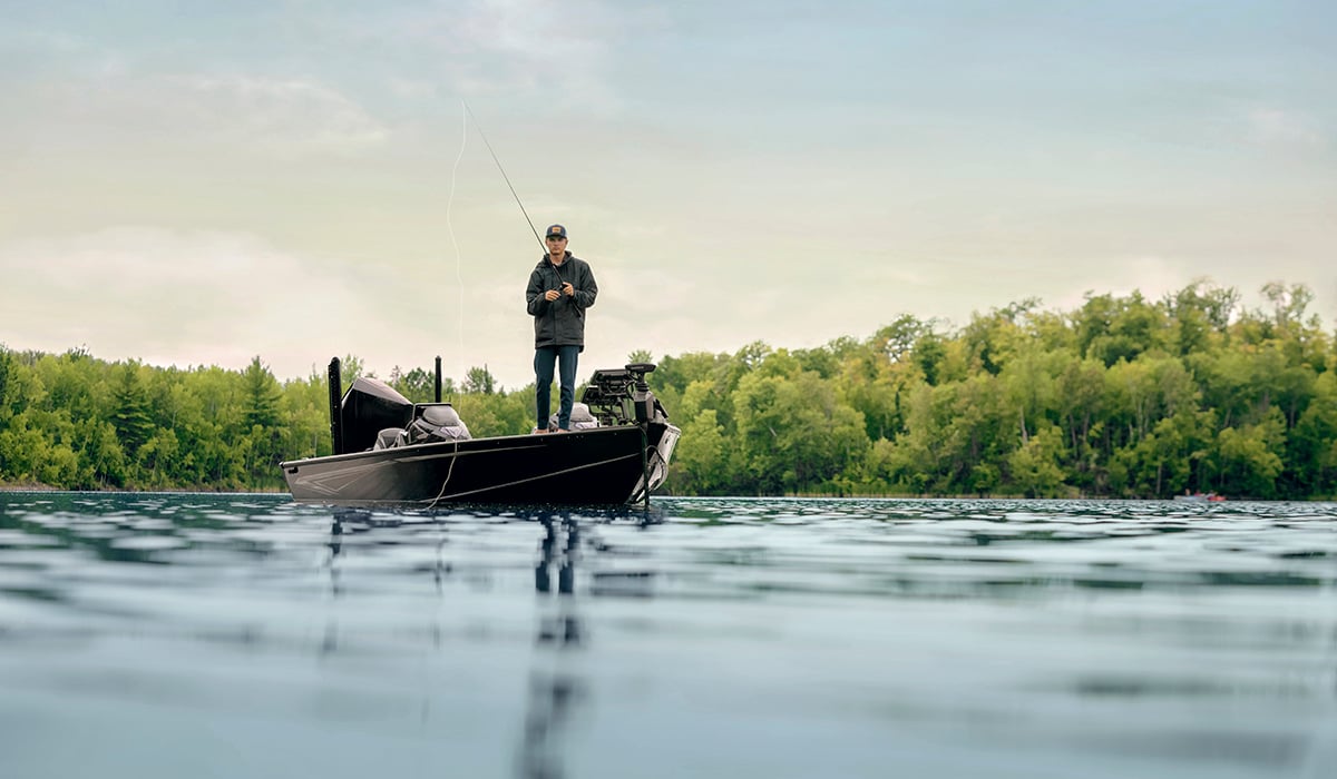 A man standing on the end of his boat with his rod in the water.