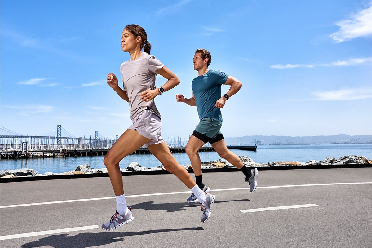A woman and a man run down a street wearing Garmin running smartwatches.