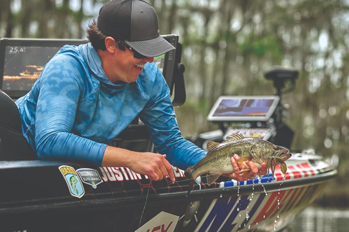 Justin Hamner smiling and holding a fish on the edge of his boat.
