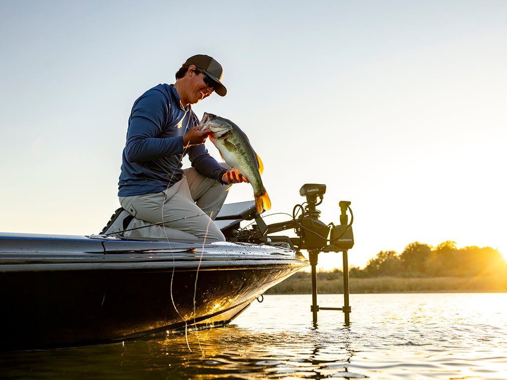 Justin Hamner kneeling at the edge of his boat holding a fish. Spy pole is attached at the end of the boat.