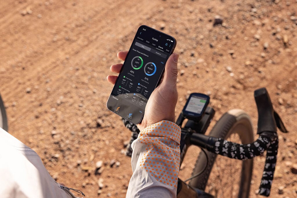 A cyclist checks their phone to view metrics, including left/right balance, from their Rally power meter.